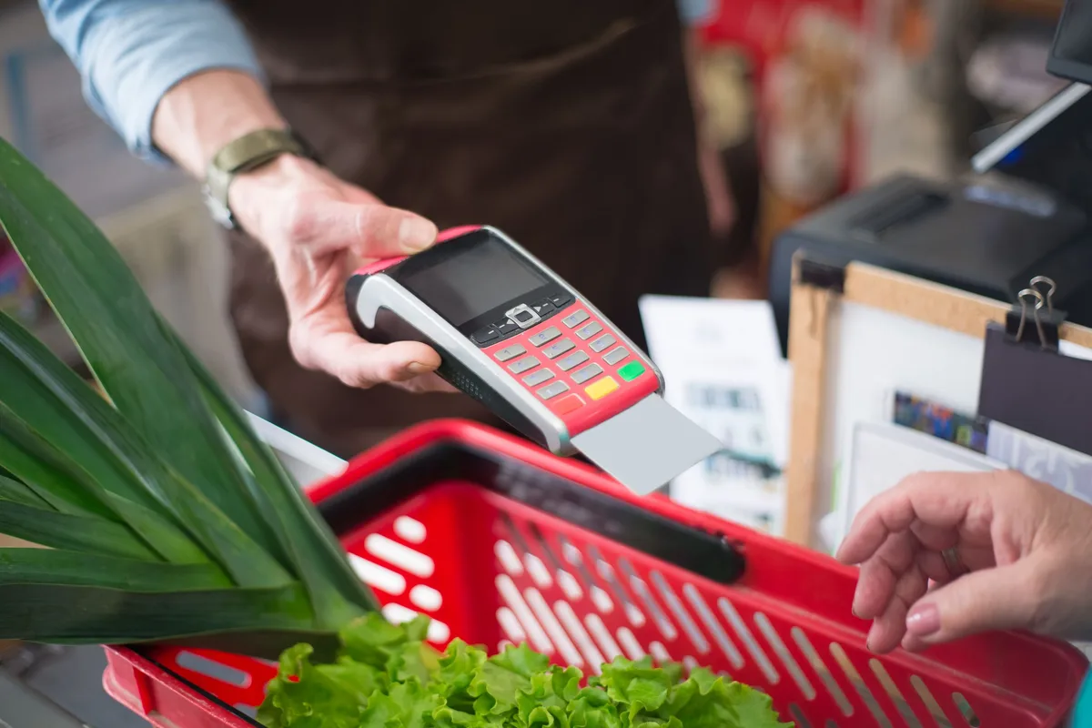 Person bezahlt an einer Supermarktkasse kontaktlos mit ihrer Karte am Terminal.