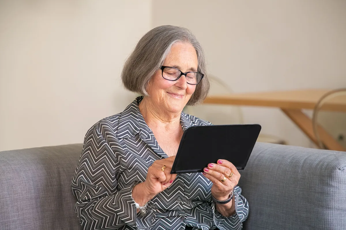 Eine ältere Frau lächelt beim Bedienen eines Tablets.
