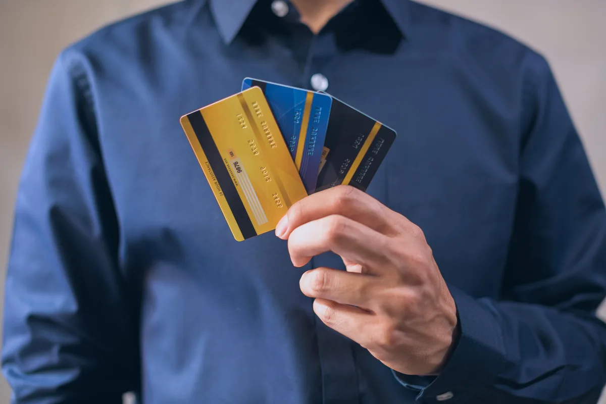 Ein Mann hält drei unterschiedliche Zahlungskarten aufgefächert in der Hand.